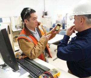 Two men look at a phone with connected maintenance data on the screen.