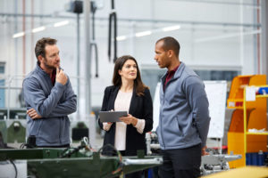 Automobile engineer discussing with colleagues in car factory. Multi-ethnic male and female professionals are standing at car production line. They are in automotive industry.